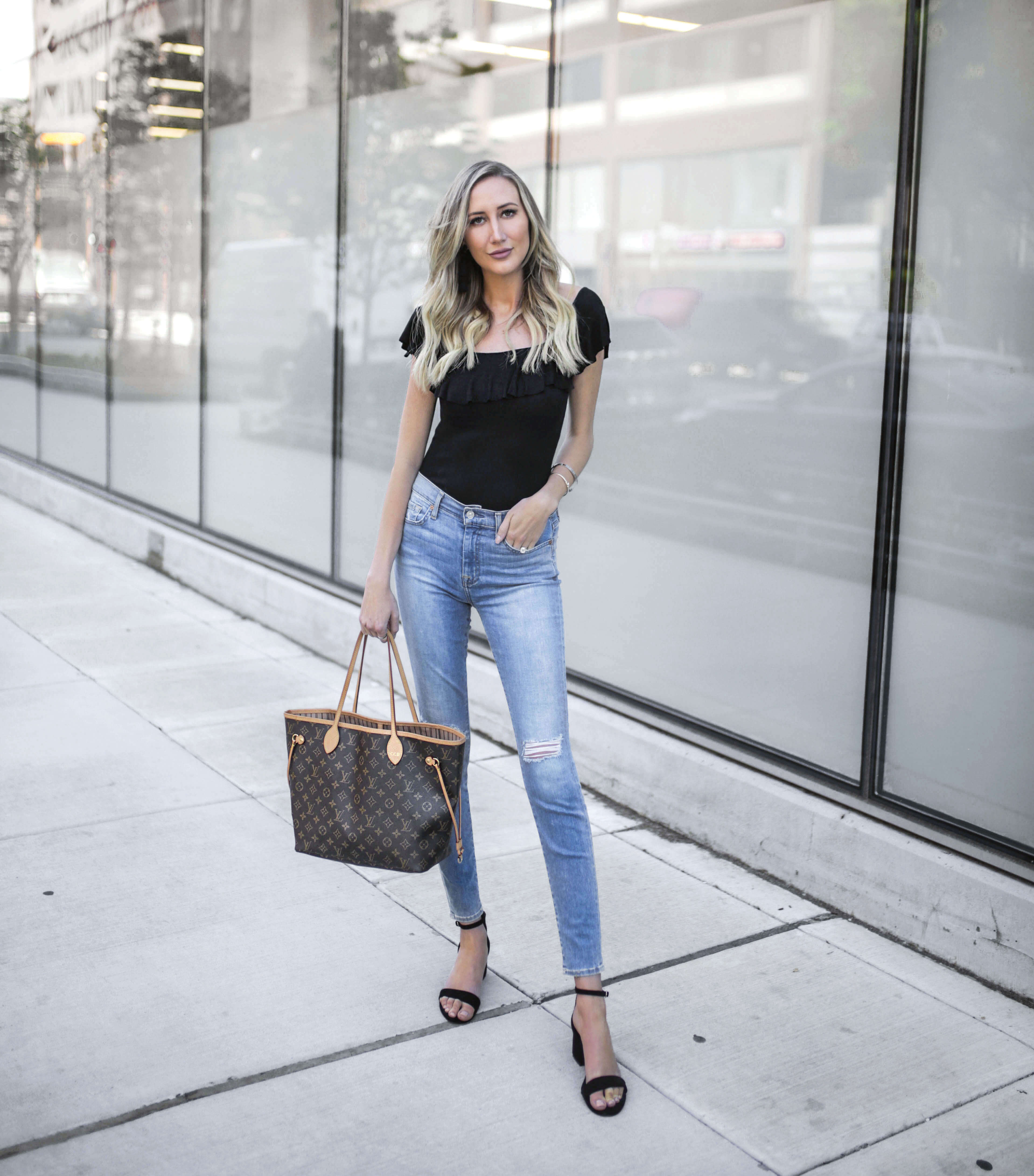 Carly Cristman wearing a black ruffle top and 7 for All Mankind denim with Louis Vuitton Neverfull bag