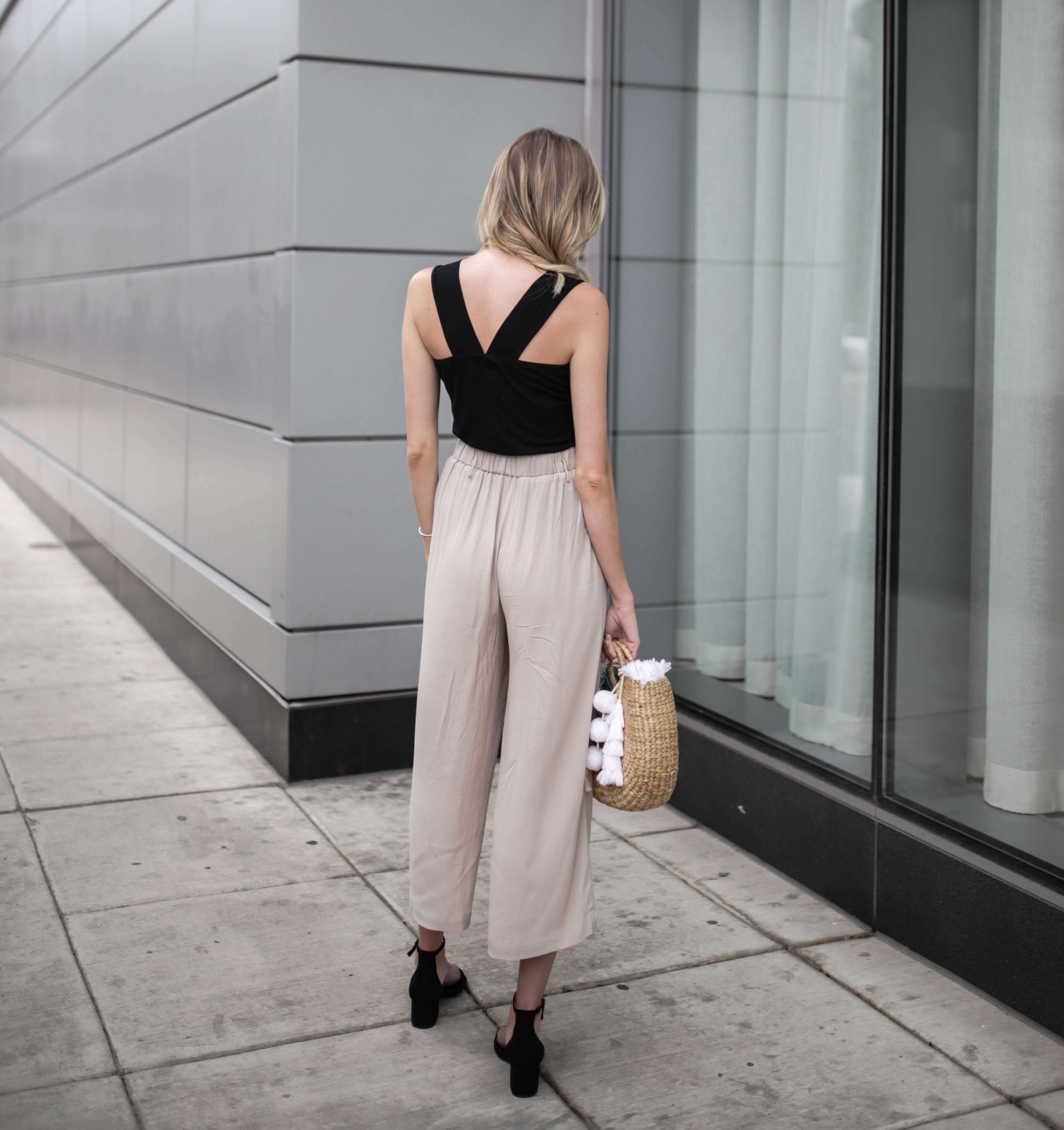 Carly Cristman wearing black tank top with taupe beige flowy cropped pants culottes. Summer outfit inspiration, basket bag, straw bags, easy summer outfits, neutral summer outfit, summer work attire