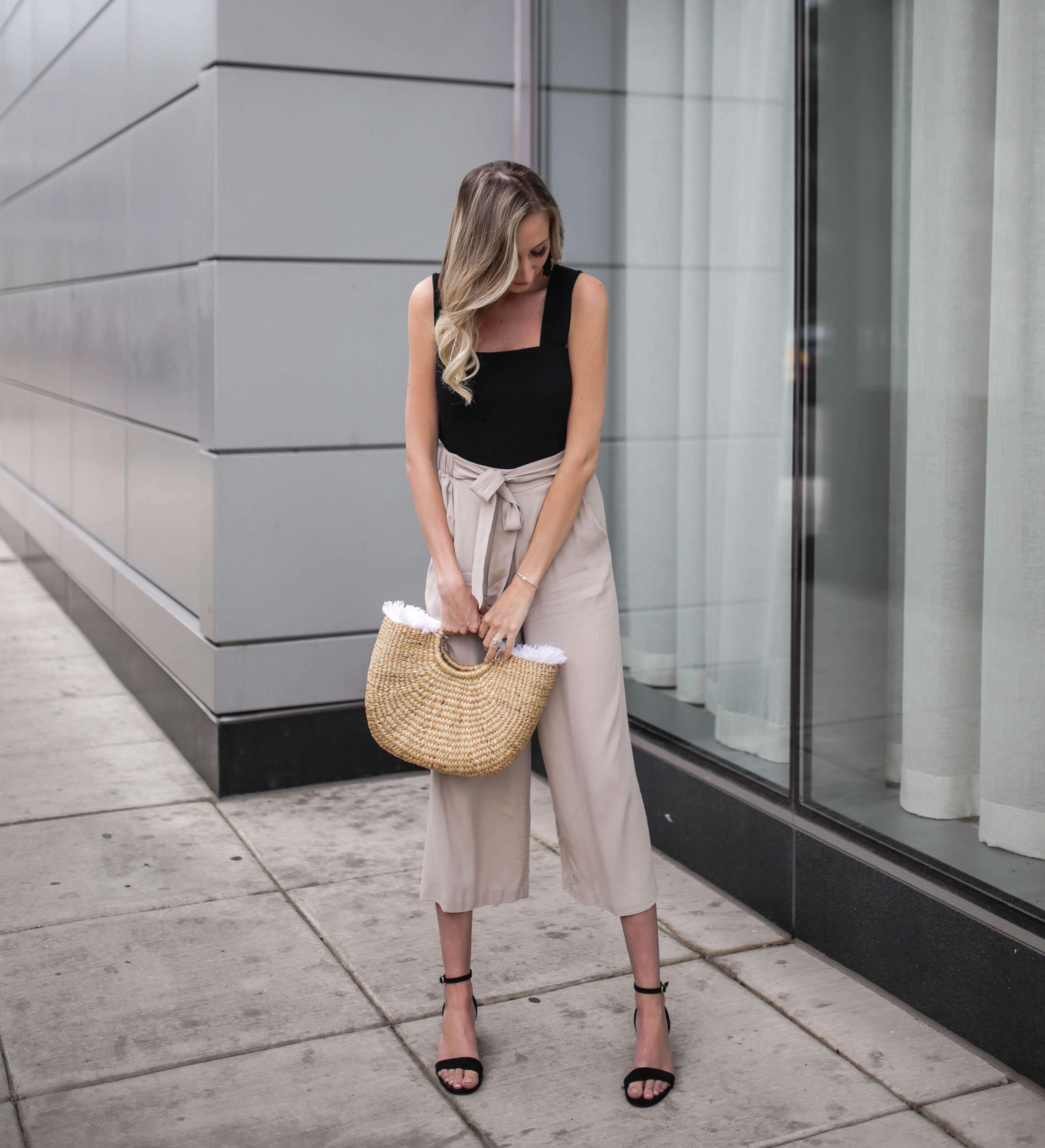 Carly Cristman wearing black tank top with taupe beige flowy cropped pants culottes. Summer outfit inspiration, basket bag, straw bags, easy summer outfits, neutral summer outfit, summer work attire